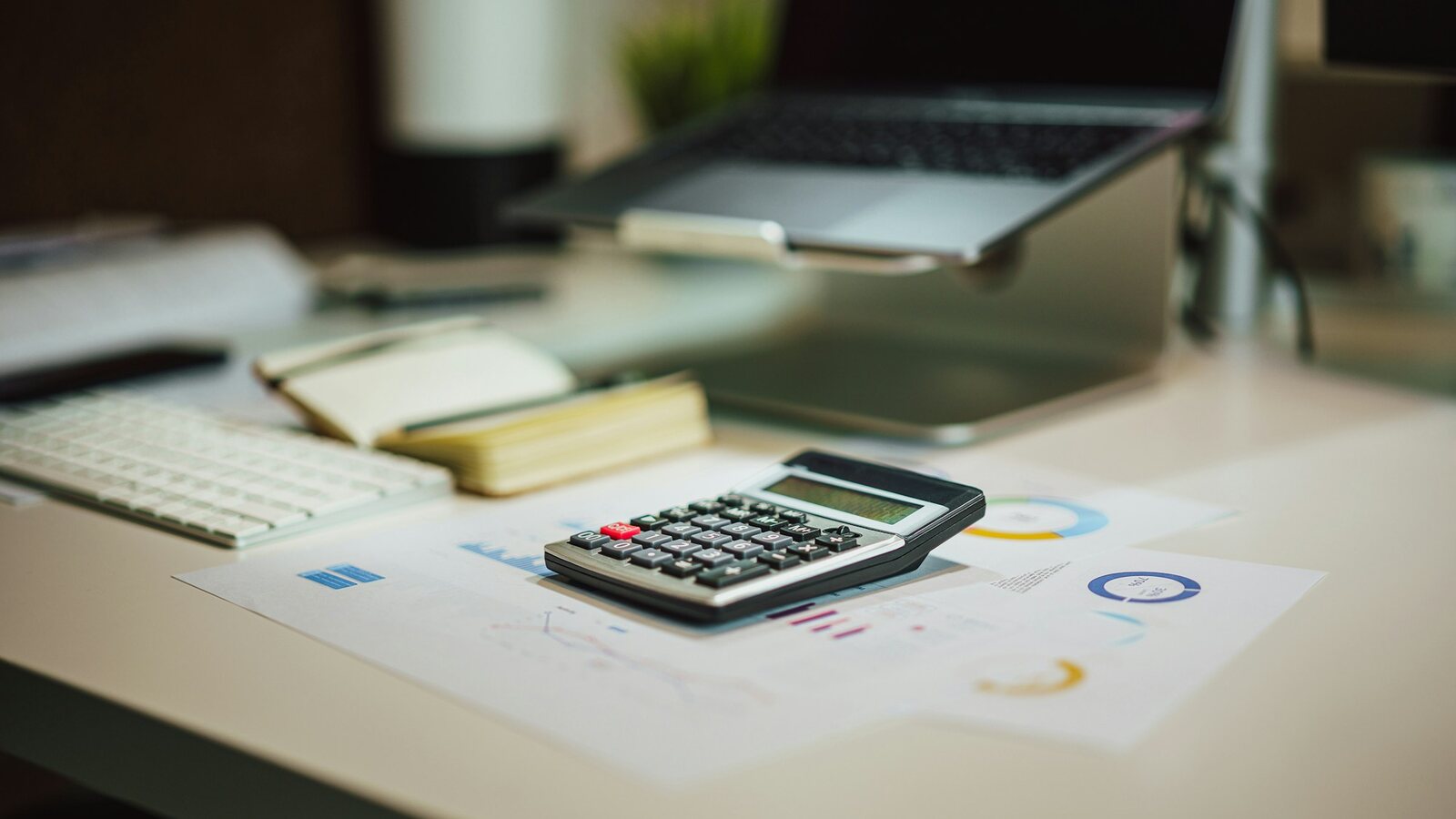 Desk with a calculator, printed figures and a laptop