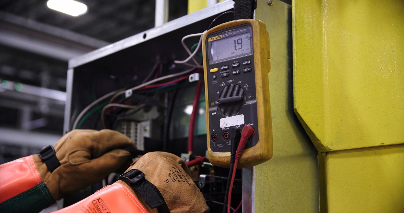 Electrician using a multimeter to check wiring inside an industrial control panel