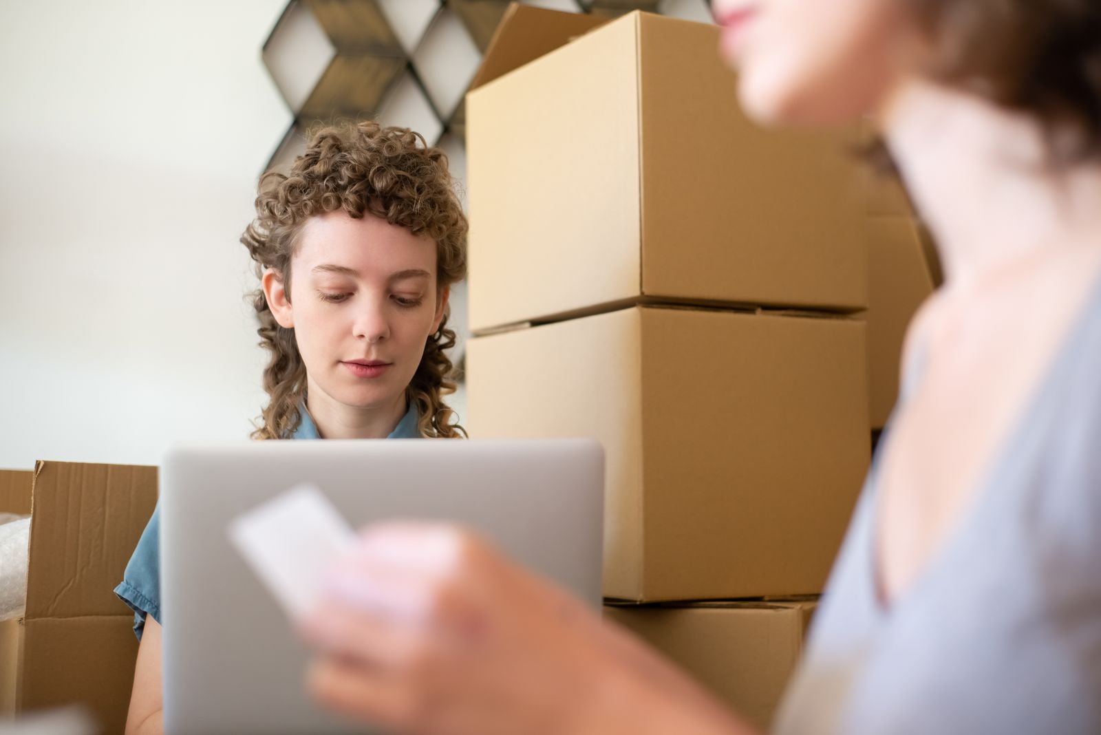 Two people surrounded by cardboard boxes checking online orders on a laptop