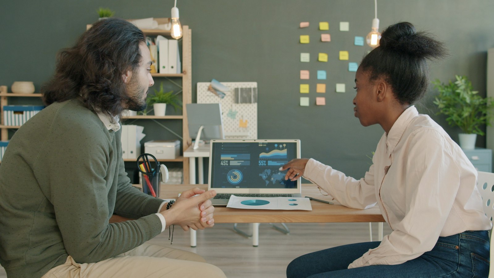 Two colleagues in an office discussing data on a laptop screen