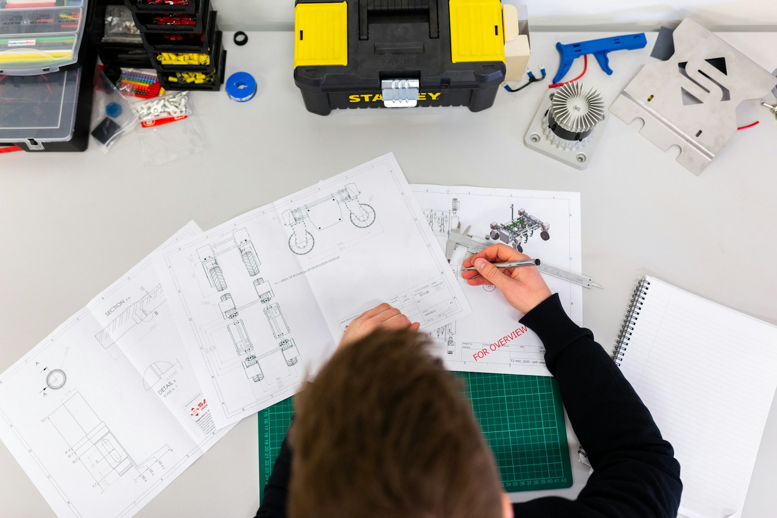 Engineer using a caliper to check measurements against a technical drawing on a desk