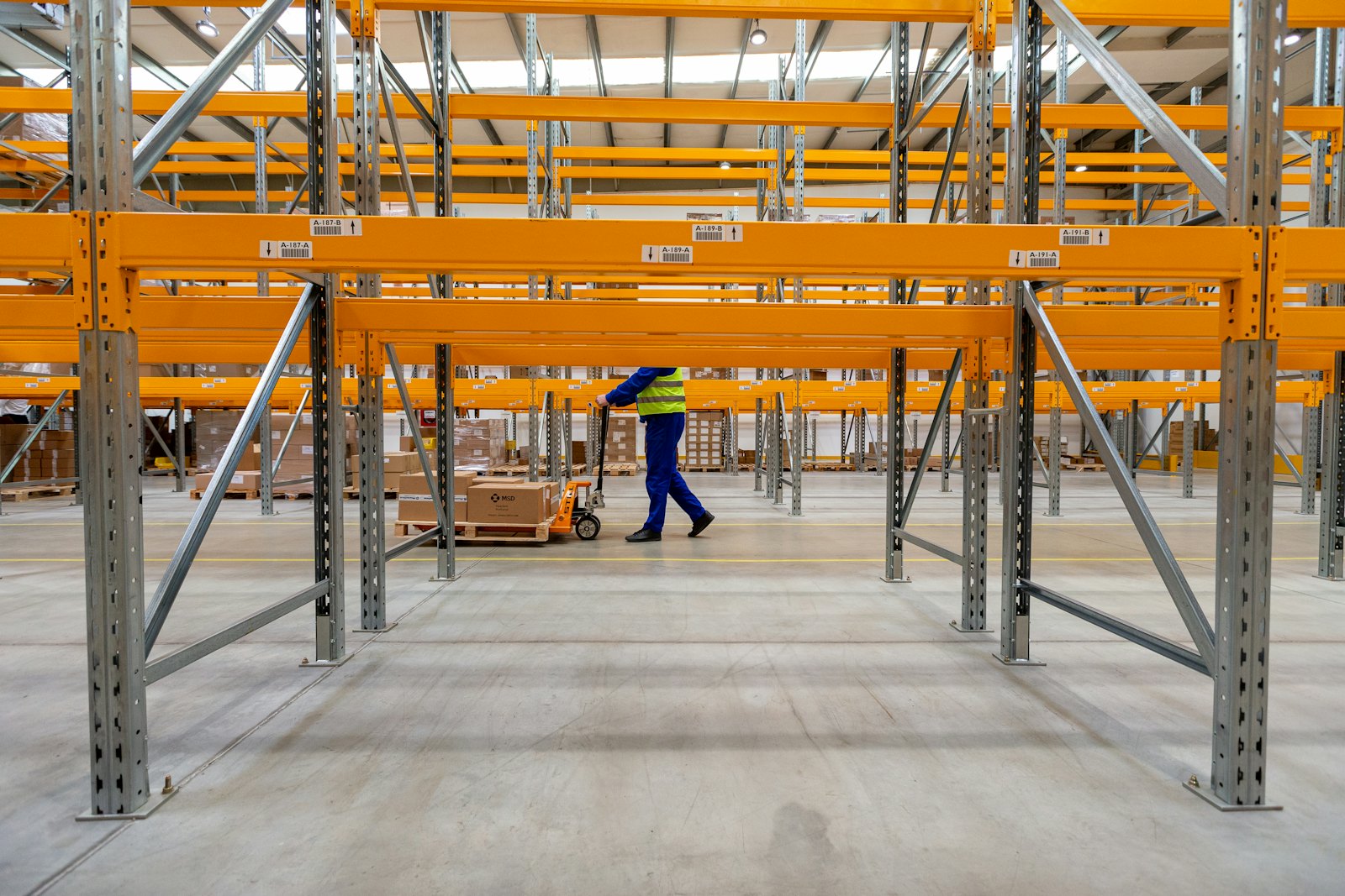 Warehouse worker walking along an aisle between tall shelving stacked with goods