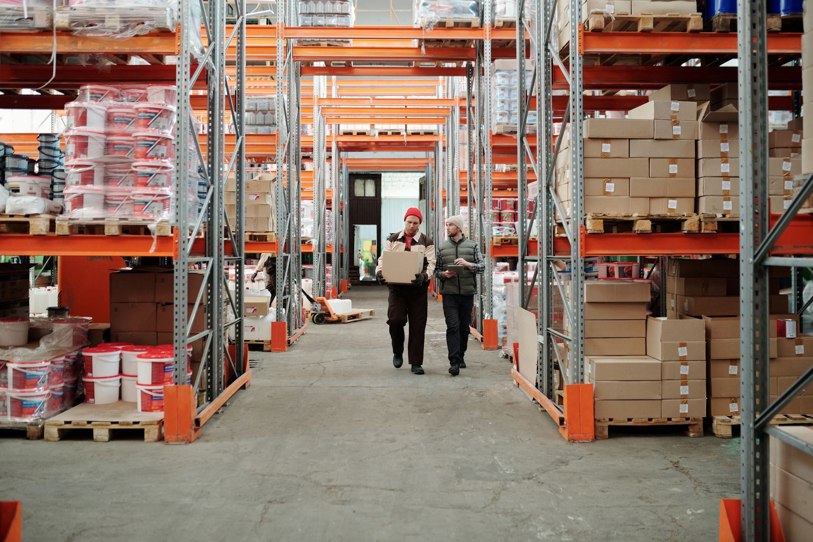 Two warehouse workers handling a package in an aisle lined with shelves of boxed stock