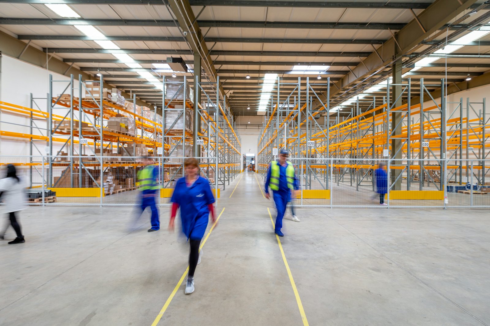 Workers walking along a warehouse aisle between stocked racking