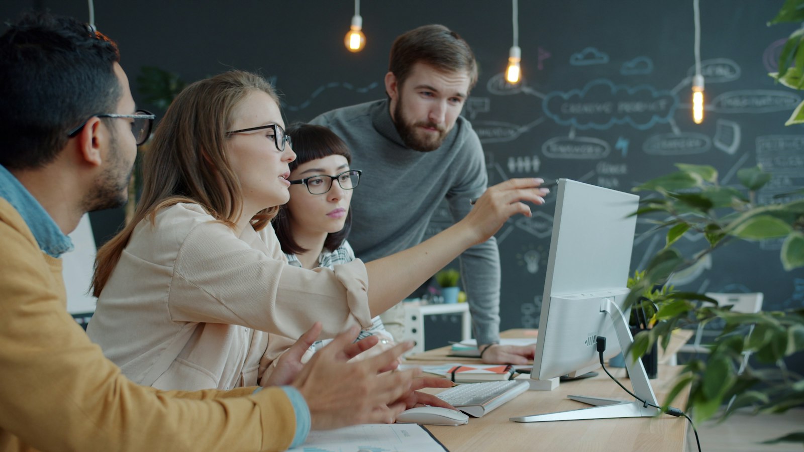 Colleagues in an open-plan office talking and pointing at a laptop screen