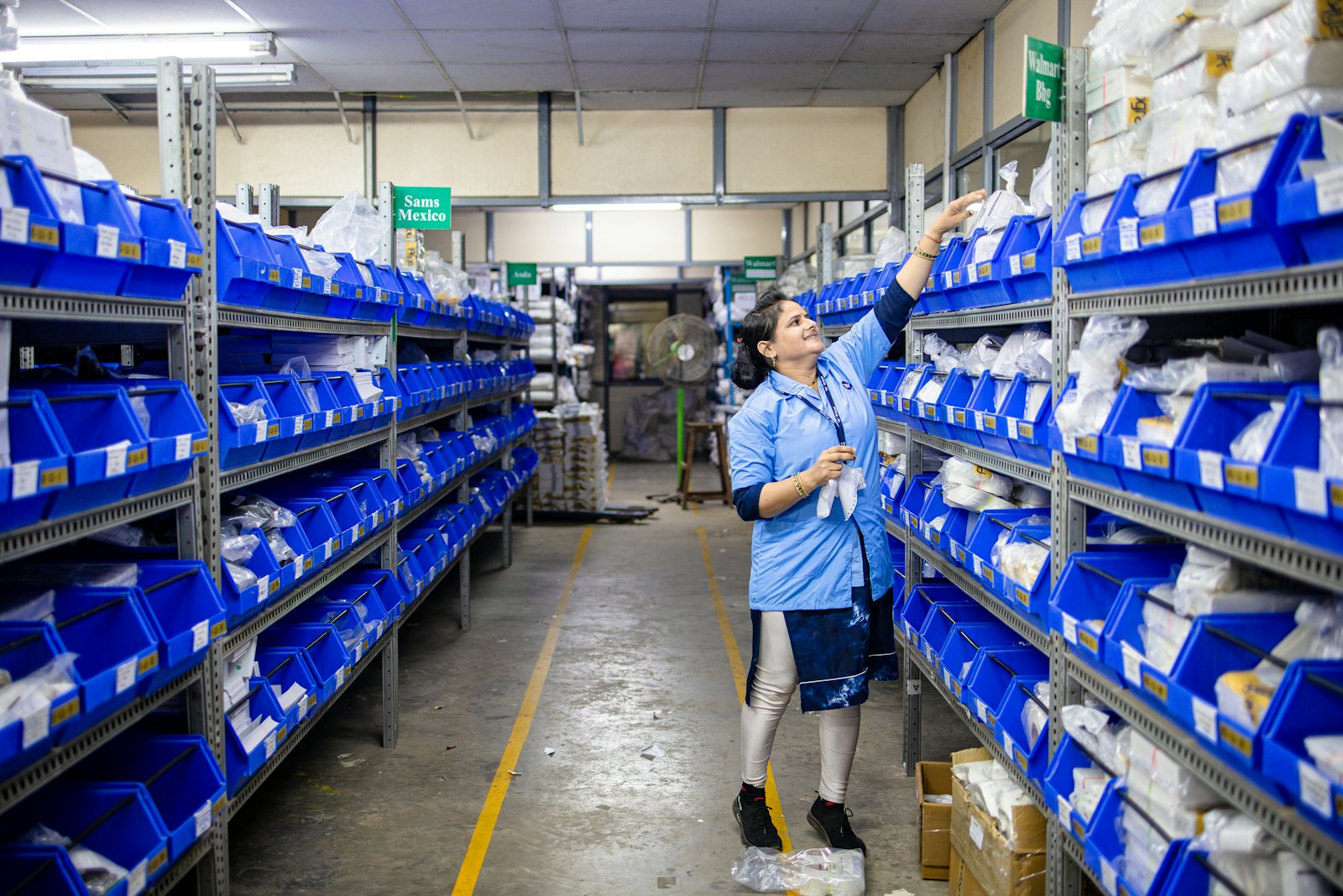 A warehouse worker reaching to take an item from a shelf in a pick aisle