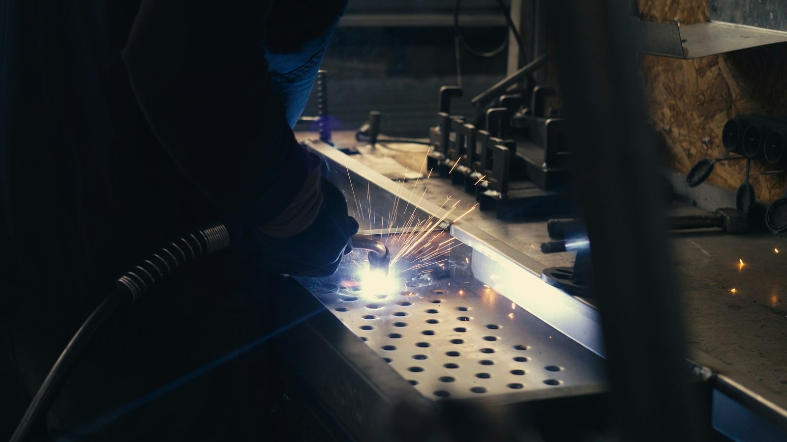 Welder working on a perforated metal sheet with sparks in a factory