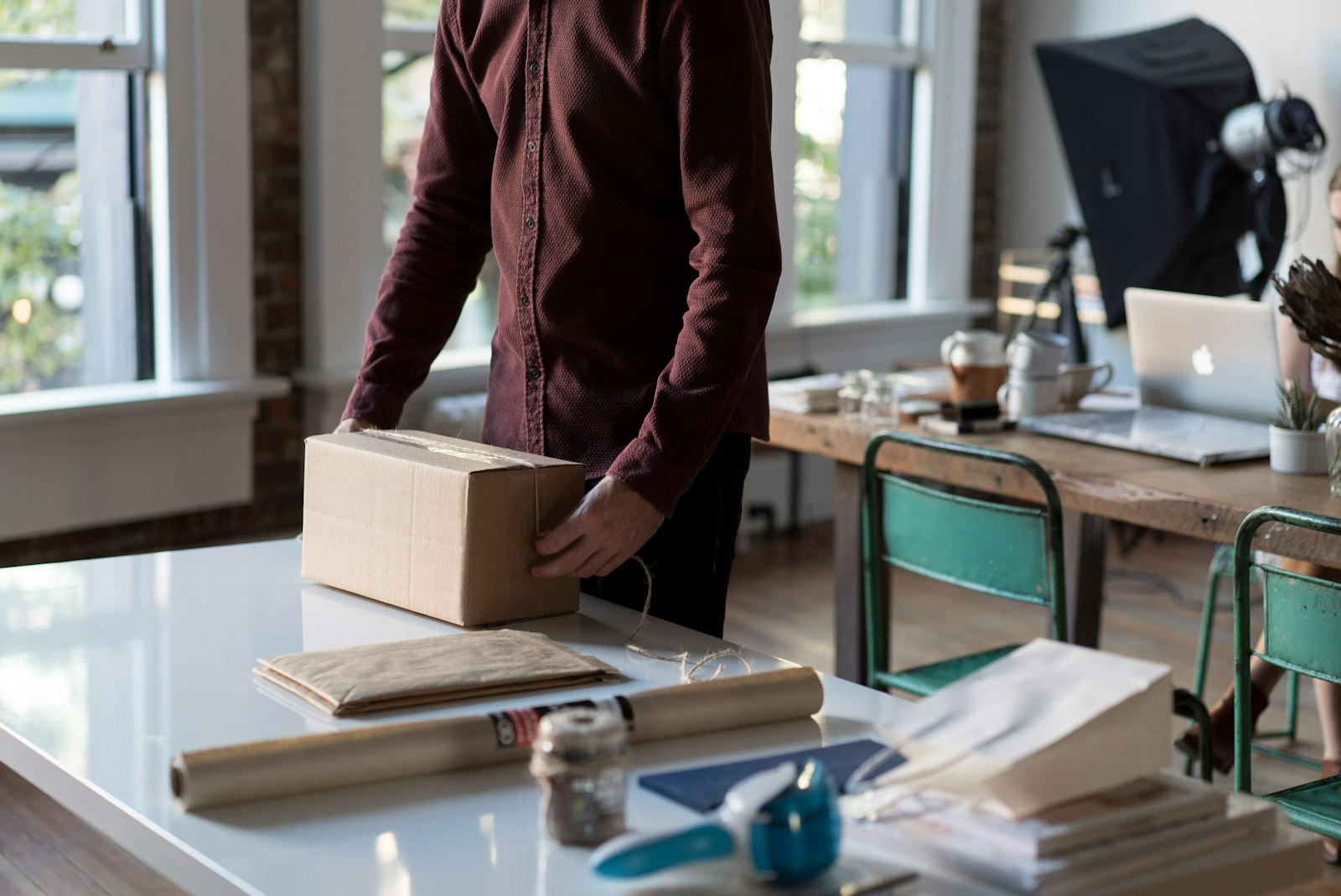 Person at a desk with a laptop holding a cardboard box ready to ship an online order