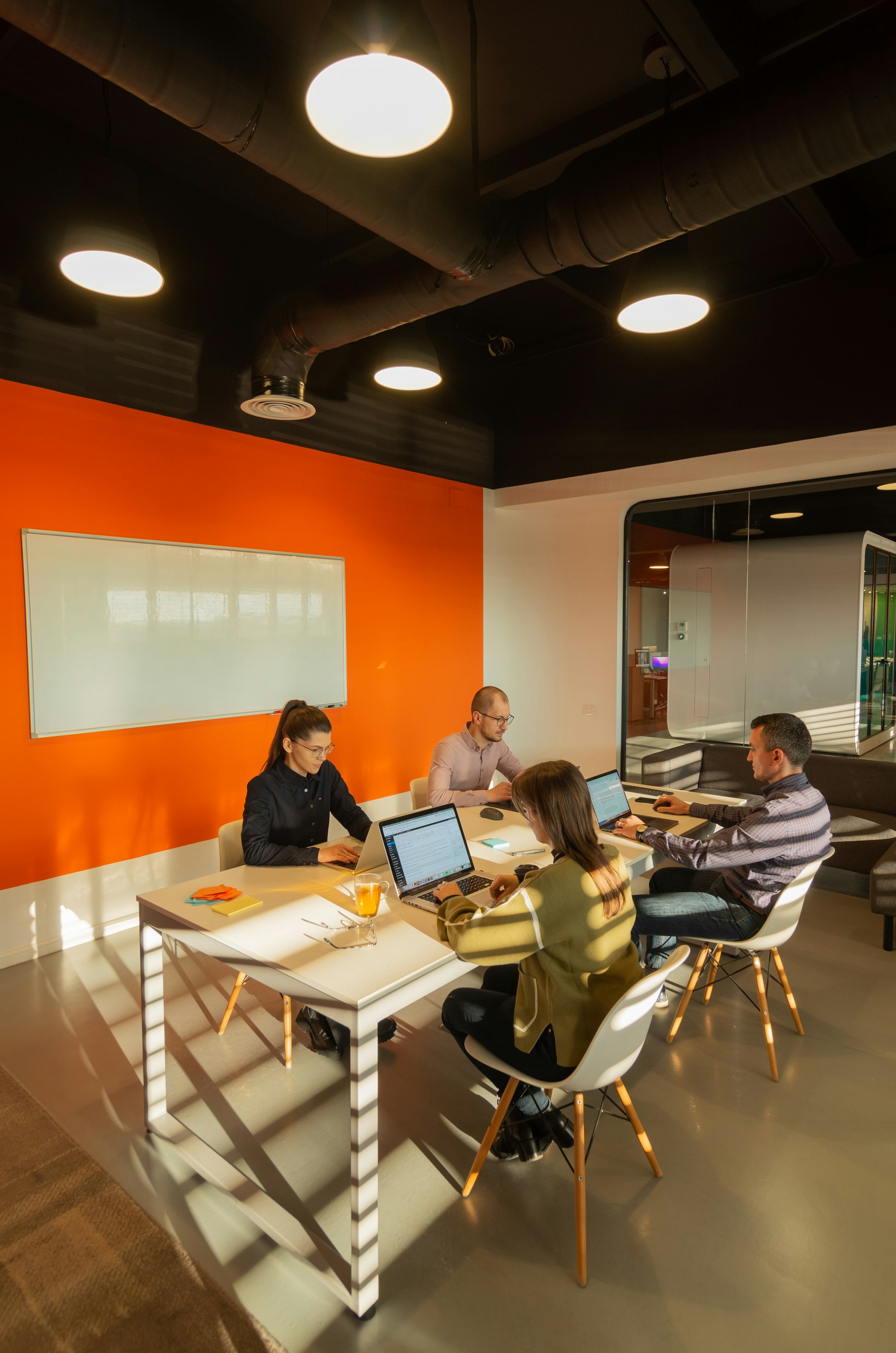 Four people working at laptops around a table in a modern meeting room